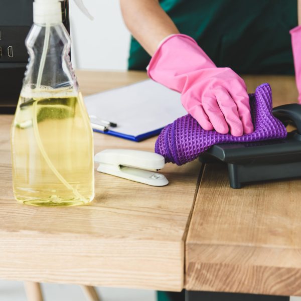 Commercial cleaner in rubber gloves cleaning telephone on table in office